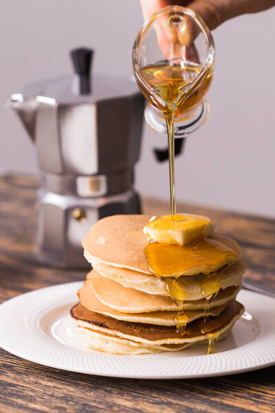 Close-up of pouring maple syrup on stack of pancakes.