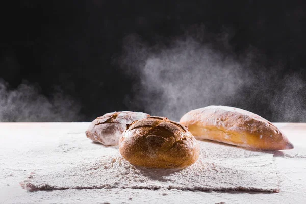 Traditionell hantverkare rågbröd limpa faller i mjöl. Mörk bakgrund. Bageri och hembakat rustikt brödkoncept. — Stockfoto