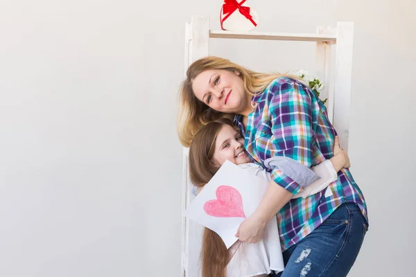 Feliz dia das mães. Filha parabeniza mãe e dá seu cartão postal. Mamãe e menina sorrindo e abraçando. Férias em família e maternidade . — Fotografia de Stock