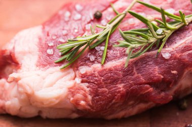 Çiğ et. Biberiye ve baharatla ahşap bir kesme tahtasının üzerinde büyük bir parça et, yakın plan..