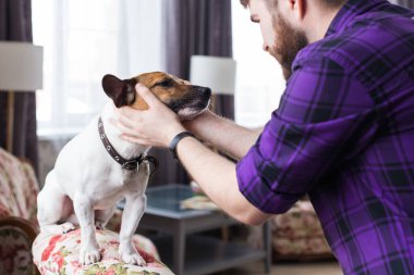 Yakından bakınca yakışıklı genç hippi adam oynuyor ve evdeki sevgili köpeğini çok seviyor. Pozitif insani duygular, yüz ifadesi, duygular.