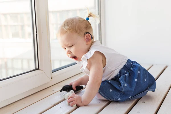 Hörapparat i flickornas öra. Ett småbarn som bär hörapparat hemma. Begreppet barn med funktionshinder, funktionshinder och dövhet. — Stockfoto