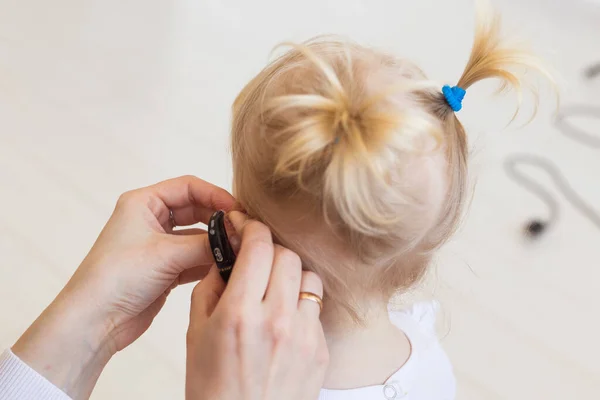 Audífono en el oído de las niñas. Niño pequeño usando un audífono en casa. Concepto de niño con discapacidad, discapacidad y sordera . — Foto de Stock