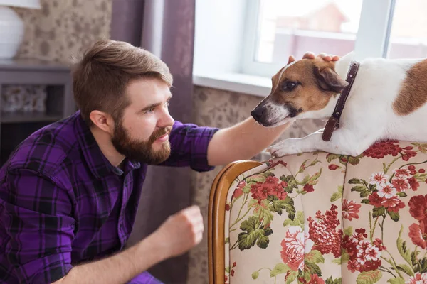 Joyeux jeune homme assis avec son chien à la maison. Propriétaire d'animal, animaux et concept d'amitié . — Photo