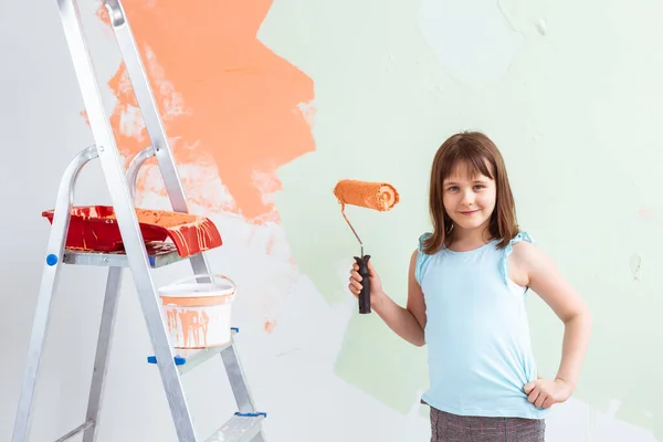 Reparación en el apartamento. La niña feliz pinta la pared con pintura naranja. Concepto de renovación y redecoración . — Foto de Stock