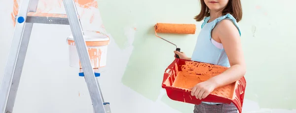 Kid standing with paint roller in hand, close-up. She is painting the wall. Redecoration, repair and repaint concept. — Stock Photo, Image