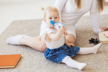 Evde elinde bir şişe maden suyu olan küçük bir kız bebek. Çocuklar ve aile kavramı.