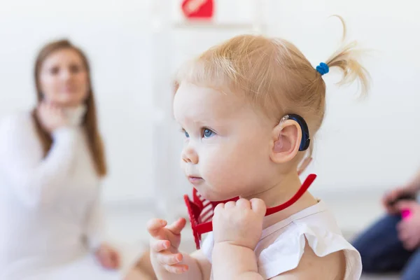 Hörapparat i flickornas öra. Ett småbarn som bär hörapparat hemma. Begreppet barn med funktionshinder, funktionshinder och dövhet. — Stockfoto