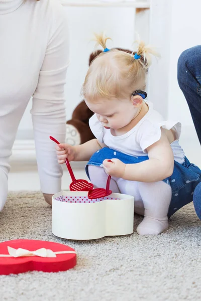 Hörapparat i flickornas öra. Ett småbarn som bär hörapparat hemma. Begreppet barn med funktionshinder, funktionshinder och dövhet. — Stockfoto