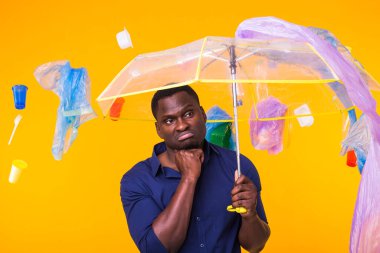 Çöp, plastik geri dönüşüm, çevre kirliliği ve ciddi bir Afro-Amerikan erkeği sarı arka planda çöp arıyor. Ekoloji hakkında düşünüyor.