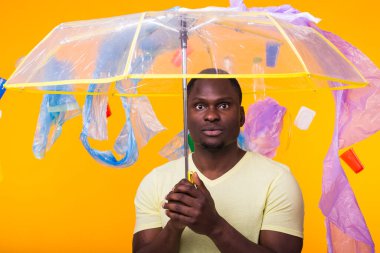 Çöp, plastik geri dönüşüm, kirlilik ve çevre konsepti sorunu - sarı arka planda çöplü dalgın Afrikalı Amerikalı adam.