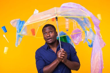Plastik geri dönüşüm sorunu, ekoloji ve çevre felaketi kavramı. Sarı arka planda çöplerle yaşayan Afro-Amerikan erkeği şaşırttı. Ekoloji felaketinden endişeleniyor.