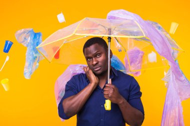 Çöp, plastik geri dönüşüm, kirlilik ve çevre konsepti sorunu - sarı arka planda çöplü dalgın Afrikalı Amerikalı adam.