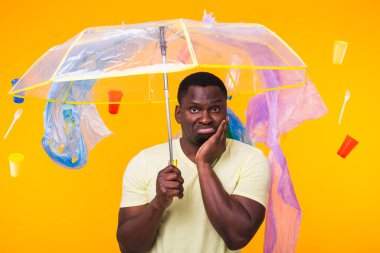 Çöp, plastik geri dönüşüm, kirlilik ve çevre konsepti sorunu - sarı arka planda çöplü dalgın Afrikalı Amerikalı adam.