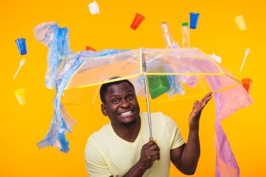 Plastik geri dönüşüm sorunu, ekoloji ve çevre felaketi kavramı. Sarı arka planda çöplerle yaşayan Afro-Amerikan erkeği şaşırttı. Ekoloji felaketinden endişeleniyor.