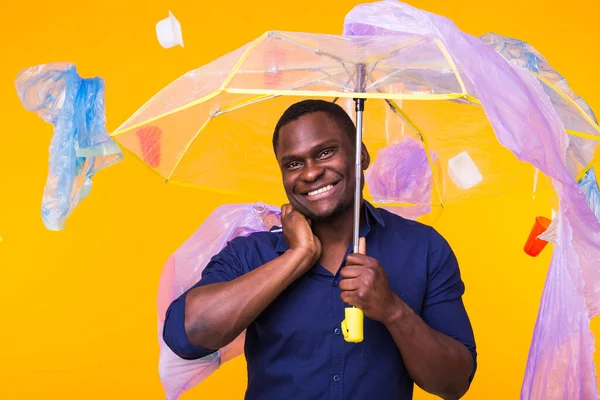 Çöp, plastik geri dönüşüm, kirlilik ve çevre konsepti sorunu - sarı arka planda çöp taşıyan komik Afrikalı Amerikalı adam.