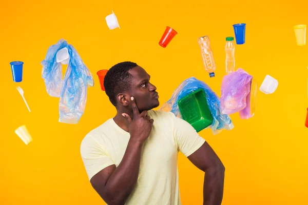 Πρόβλημα με τα σκουπίδια, την ανακύκλωση πλαστικών, τη ρύπανση και την περιβαλλοντική έννοια - Αφρικανός Αμερικανός άνθρωπος στέκεται κάτω από τα σκουπίδια σε κίτρινο φόντο — Φωτογραφία Αρχείου