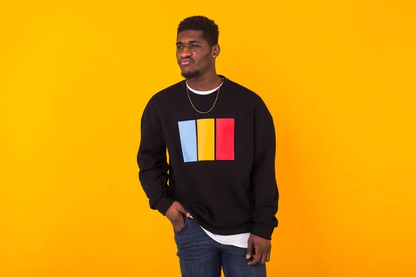 Handsome African American man posing in black sweatshirt on a yellow background. Youth street fashion photo with afro hairstyle. — Stock Photo, Image