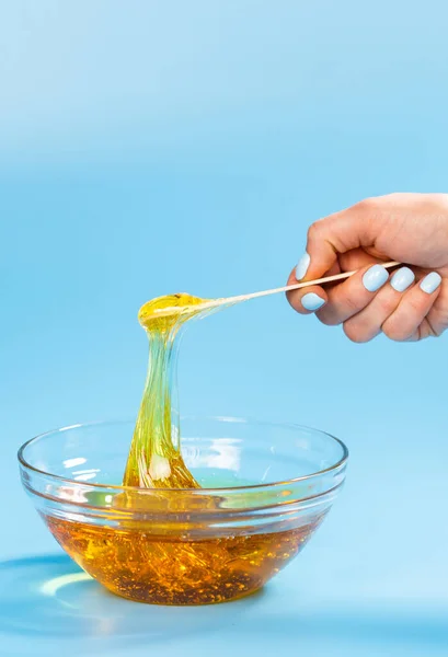 Kvinnliga händer ta ut socker pasta för socker med en trä spatel på blå bakgrund. Epilering och hårborttagning koncept. — Stockfoto