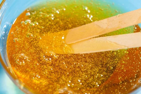 Flytande gul pasta för socker och pinnar på blå bakgrund. Hårborttagning och hårborttagning. — Stockfoto