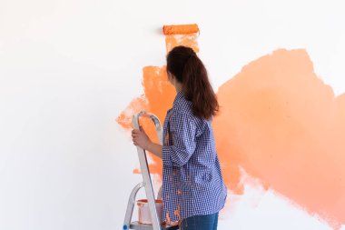 Kapalı mekanda boya pateniyle güzel bir bayan. Dekorasyon, yenileme, apartman onarımı ve ferahlatıcı konsept.