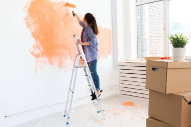 Yenileme, yeniden dekorasyon ve onarım konsepti - Yeni evde duvarları boyayan neşeli kadın.