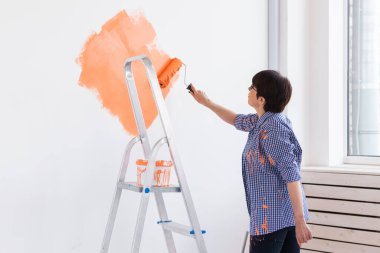 Gülümseyen orta yaşlı kadın evin içini boyuyor. Yenileme, onarım ve yeniden dekorasyon konsepti.