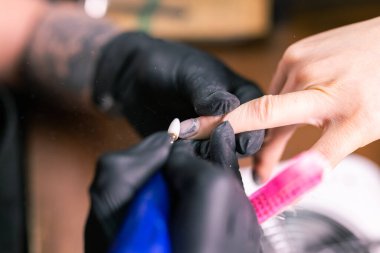 Manikürcü kadının yakın çekimi, manikür makinesi kullanarak müşterilerin tırnaklarındaki jöle parlatmasını kaldırıyor. Manikür ustası güzellik salonunda elektrikli tırnak matkabıyla çalışıyor. Donanım manikür süreci.