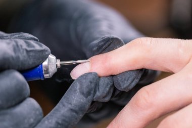 İşlem manikürü yakın çekim. Donanım manikürü için hazırlık. Lastik eldivenli güzellik uzmanı tırnak derisini kesip çivileri işliyor..