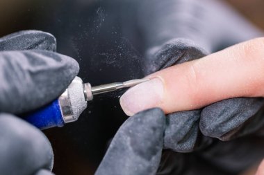 Güzellik salonunda hırdavatçı manikürü. Kadın manikürcü kadın parmaklarına manikür yapmak için elektrikli tırnak matkabı uyguluyor. Mekanik manikür yakın plan. Vücut bakımını kabul et.