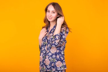 Moda portresi. Evdeki güzel kız. Pijama giyip renkli sarı arka planda eğleniyor..