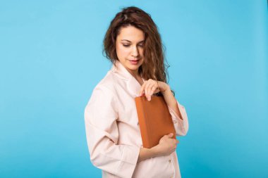 Genç kız mavi arka planda pijamalarıyla kitap okuyor. Rahatla iyi ruh hali, yaşam tarzı ve uyku kıyafetleri konsepti.