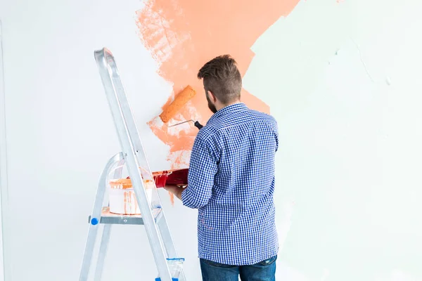 Boldog ember fest belső fal festék görgő az új házban. Egy görkoris fickó, aki festéket hord a falra. Visszanézés. — Stock Fotó