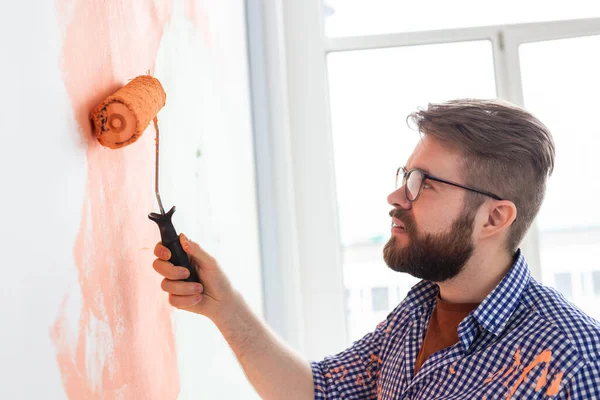 Egy férfi festőhengerrel idebent. Újjáépítés, felújítás, lakásjavítás és felújítás koncepciója. — Stock Fotó