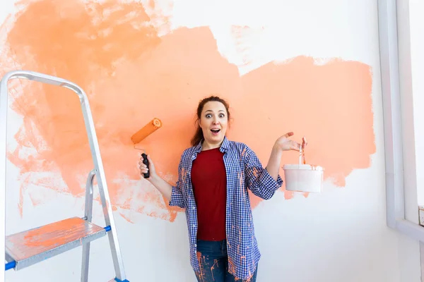 Funny smiling woman painting interior wall of home with paint roller. Redecoration, renovation, apartment repair and refreshment concept. — Stock Photo, Image