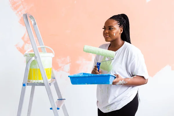 Bella giovane donna afroamericana con rullo pittura al coperto. Ristrutturazione, ristrutturazione, riparazione di appartamenti e concetto di ristoro . — Foto Stock