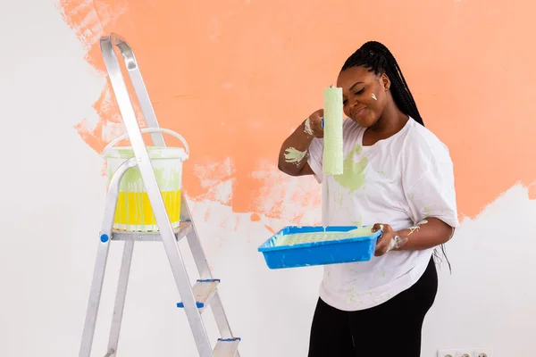 Bella giovane donna afroamericana con rullo pittura al coperto. Ristrutturazione, ristrutturazione, riparazione di appartamenti e concetto di ristoro . — Foto Stock
