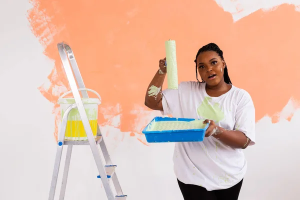 Giovane donna afro-americana felice pittura parete interna con rullo di vernice in nuova casa. Una donna con rullo che applica vernice su un muro. — Foto Stock
