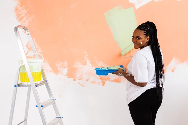 Piuttosto sorridente donna afroamericana pittura parete interna della casa con rullo di vernice. Ristrutturazione, ristrutturazione, riparazione di appartamenti e concetto di ristoro. — Foto Stock