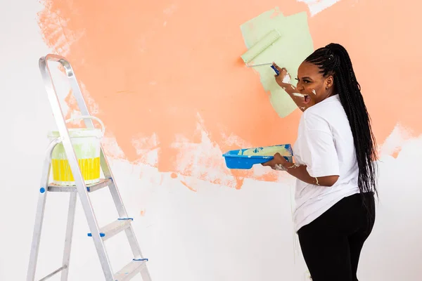 Donna afro dipingere le pareti della nuova casa. Concetto di ristrutturazione, riparazione e ridecorazione. — Foto Stock