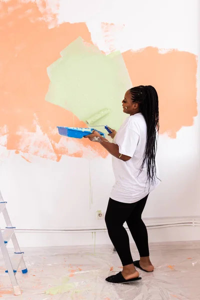 Bella casalinga afroamericana che dipinge il muro. Concetto di ristrutturazione, ridecorazione e riparazione. — Foto Stock