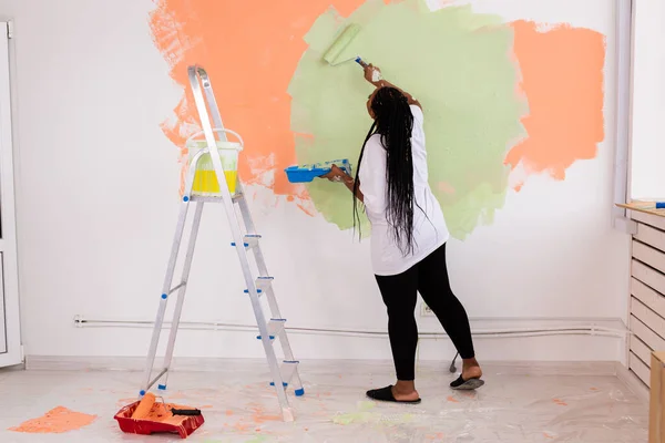 Bella ragazza afro-americana dipingere il muro con rullo di vernice. Ritratto di una giovane bella donna che dipinge un muro nel suo nuovo appartamento. Concetto di ristrutturazione e riqualificazione . — Foto Stock