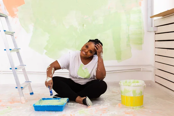 Felice donna afro-americana sorridente pittura parete interna della nuova casa. Ristrutturazione, ristrutturazione, riparazione di appartamenti e concetto di ristoro . — Foto Stock