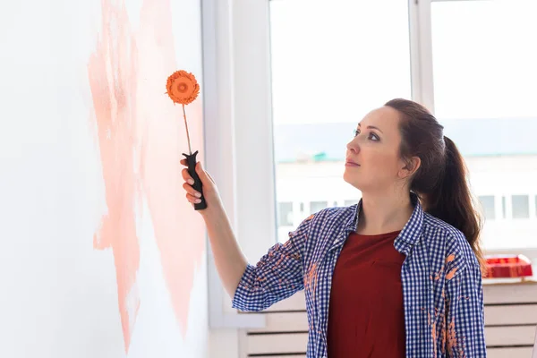 Glückliche junge Frau bemalt Innenwand mit Farbroller im neuen Haus. Eine Frau mit Walze trägt Farbe auf eine Wand auf. — Stockfoto