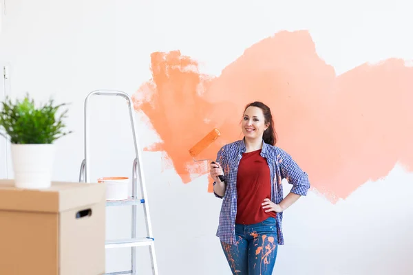 Feliz mujer sonriente pintando la pared interior de la casa nueva. Redecoración, renovación, reparación de apartamentos y concepto de refresco. — Foto de Stock