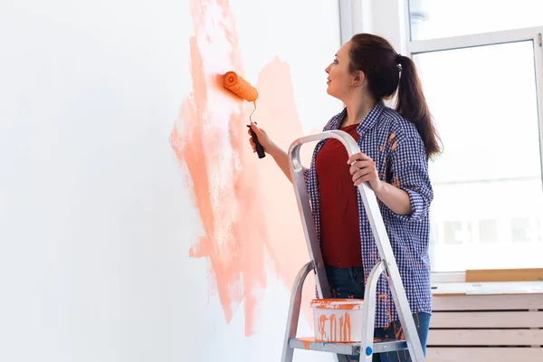 Yeni evin duvarlarını boyayan neşeli bir kadın. Yenileme, onarım ve yeniden dekorasyon konsepti. — Stok fotoğraf