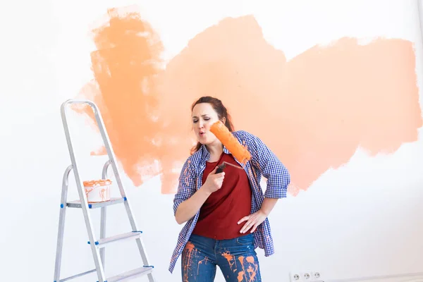 Bailando divertida mujer sonriente pintando la pared interior de la casa nueva. Redecoración, renovación, reparación de apartamentos y concepto de refresco . — Foto de Stock