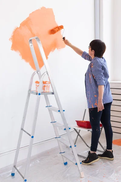 Happy smiling middle-aged woman painting interior wall of new house. Redecoration, renovation, apartment repair and refreshment concept. — Stock Photo, Image