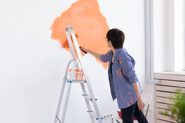 Orta yaşlı bir kadın yeni evin duvarlarını boyuyor. Yenileme, onarım ve yeniden dekorasyon konsepti. — Stok fotoğraf
