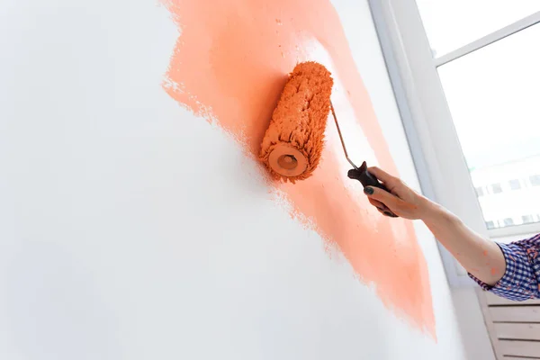 Close up woman painting wall in her new apartment. Renovation, redecoration and repair concept.